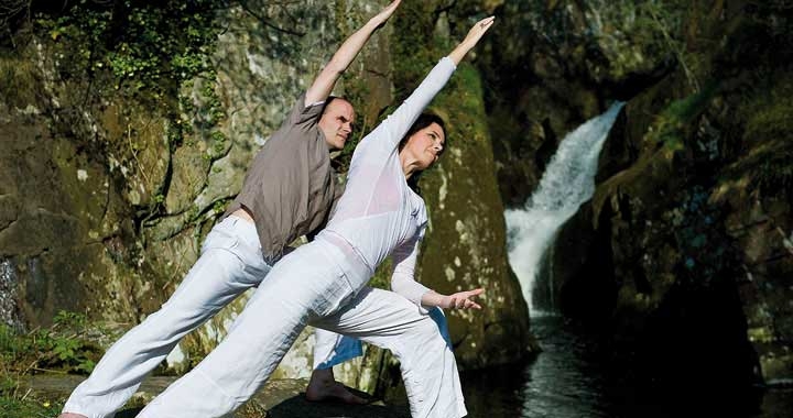 two people doing yoga by waterfall