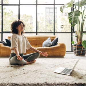 Young multiracial latina woman meditating at home with online video meditation lesson using laptop.