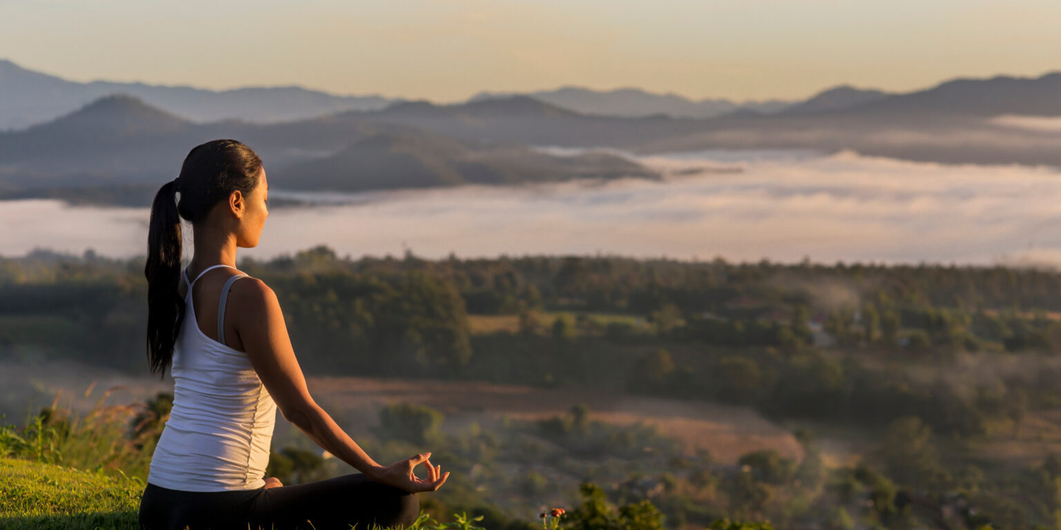 Side view of woman meditating while sitting on grassy field against sky