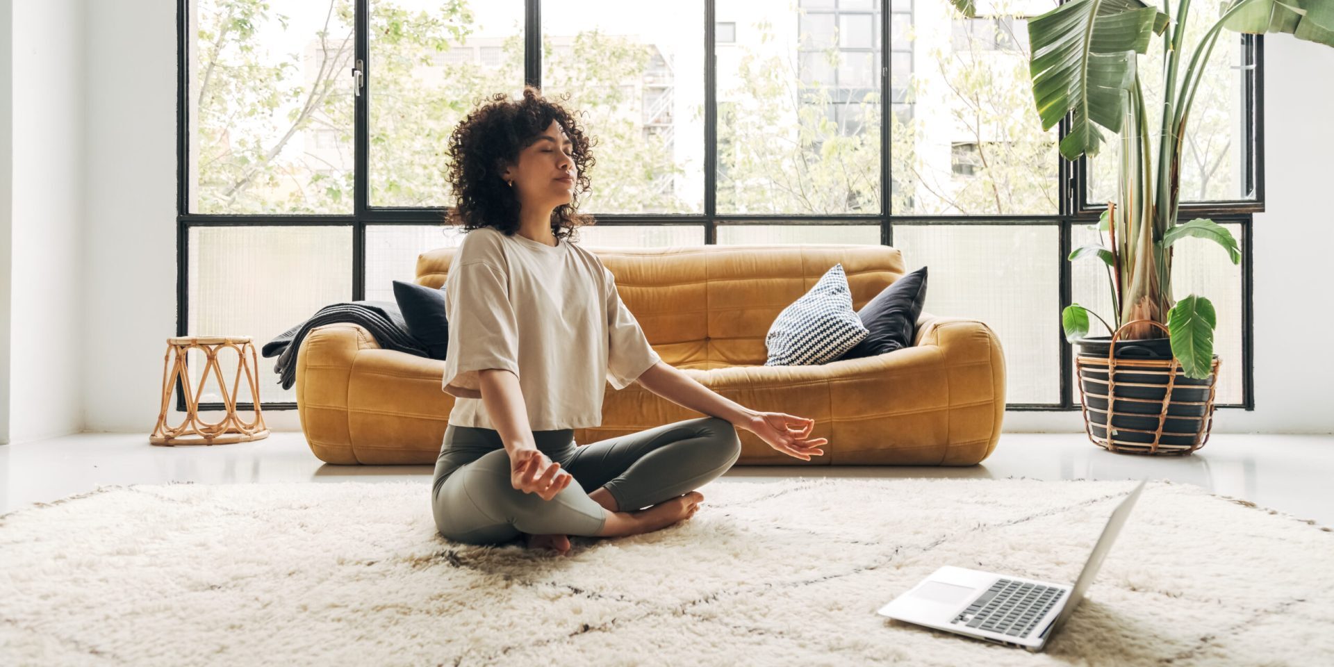Young multiracial latina woman meditating at home with online video meditation lesson using laptop. Meditation and spirituality concept.